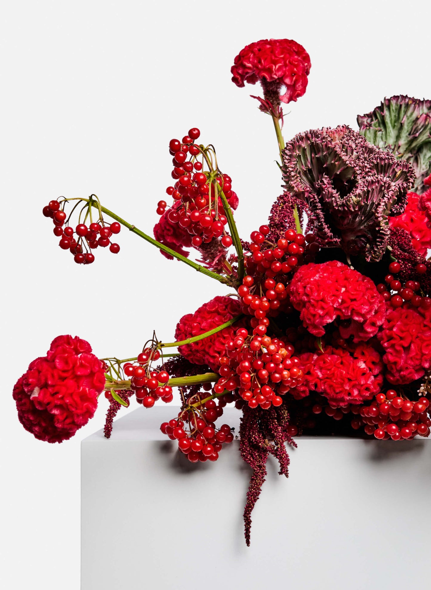 Bespoke flower arrangement. A strong red tone flower table arrangement features celosia cristata, lilies, berries and seasonal side flowers.