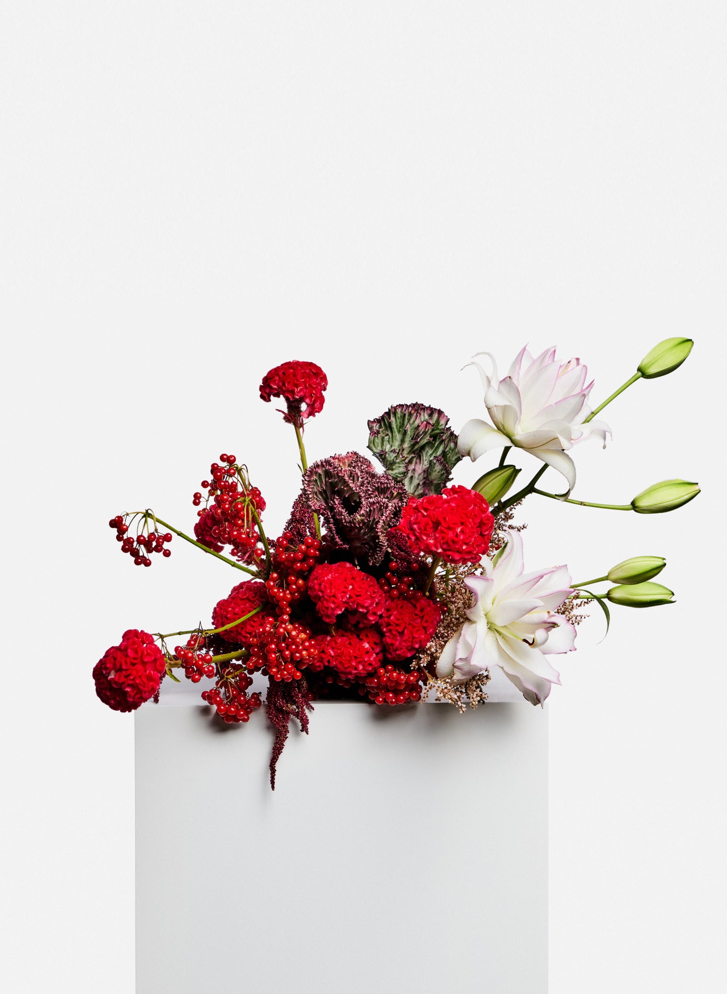 Bespoke flower arrangement. A strong red tone flower table arrangement features celosia cristata, lilies, berries and seasonal side flowers.