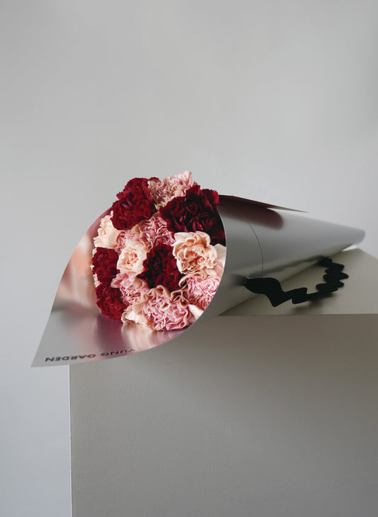 優雅的母親節花束，包含粉色, 肉色和红色康乃馨，包裹在簡约有質感的銀色包裝纸中。