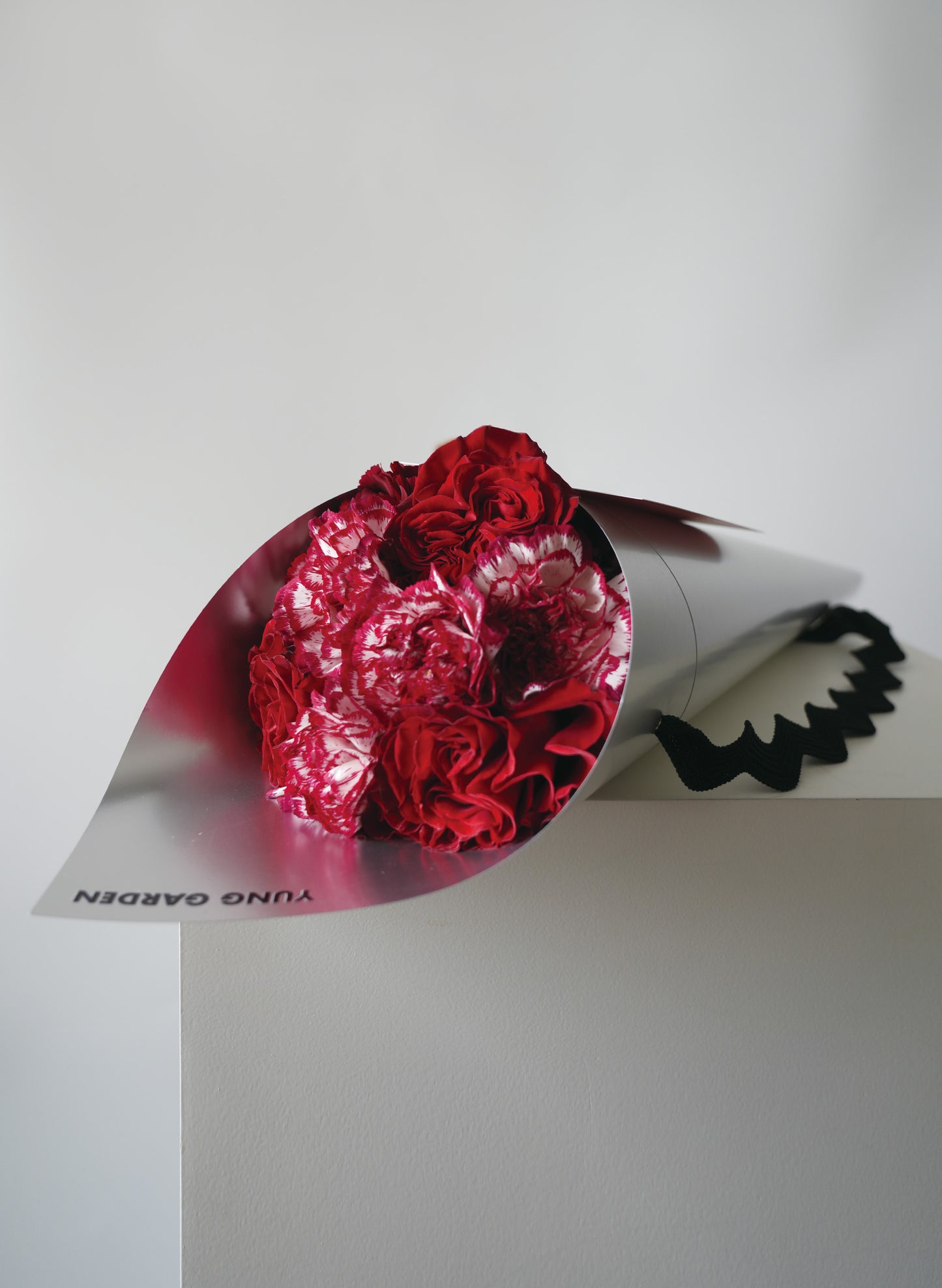 紅色玫瑰和康乃馨母親節花束，包裹在銀色印有"YUNG GARDEN"牌子名稱的包裝纸中。