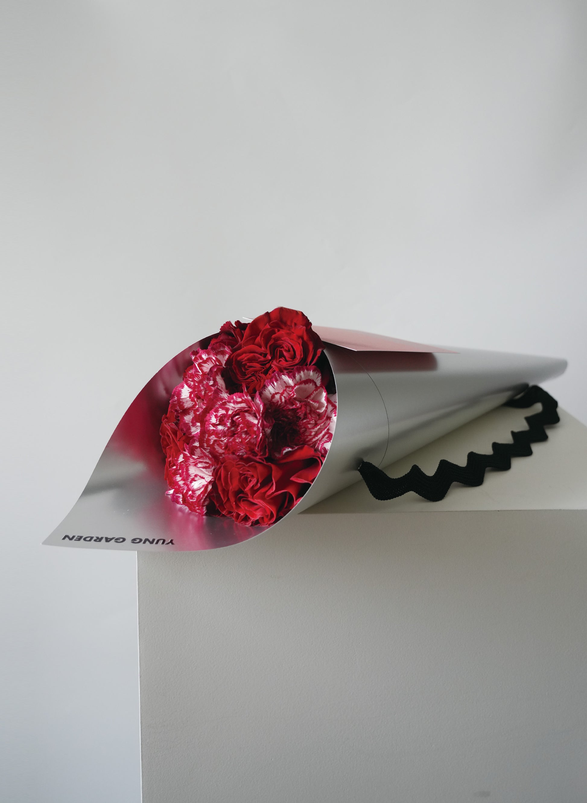 紅色玫瑰和康乃馨母親節花束，包裹在銀色印有"YUNG GARDEN"牌子名稱的包裝纸中。